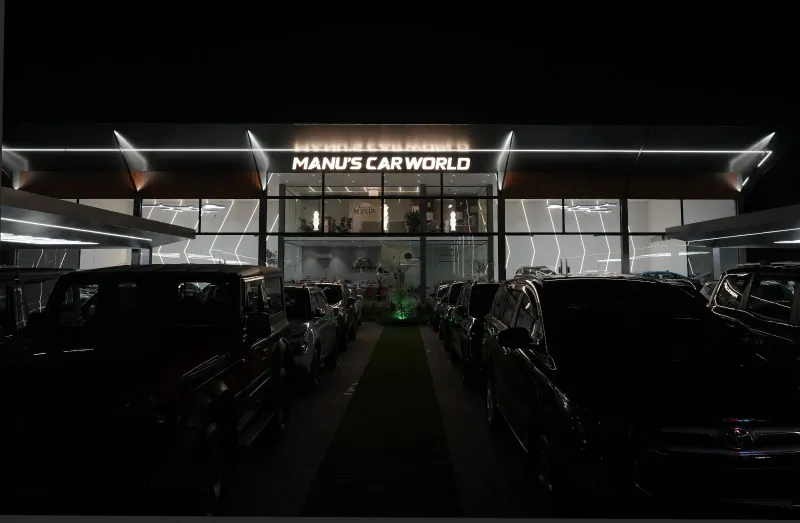 Manu's Car World showroom exterior and vehicle display at night